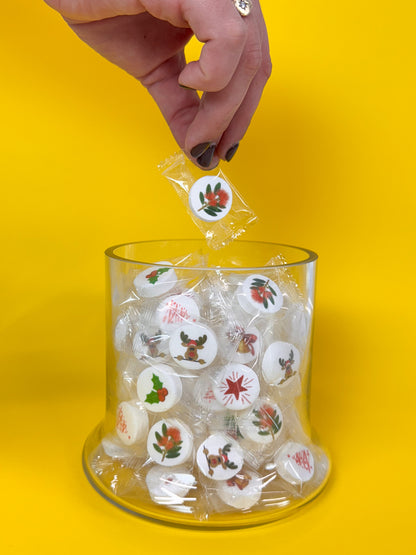 Hand placing a christmas mint into a glass container on a yellow background