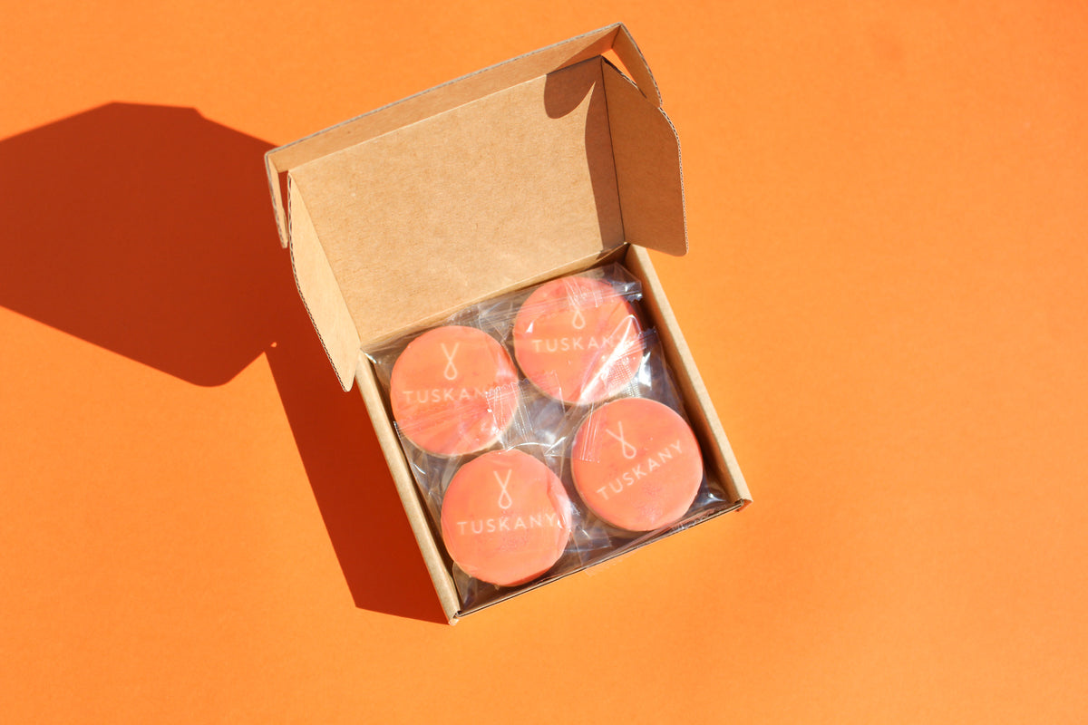 Open box containing round pink products with branding on an orange background